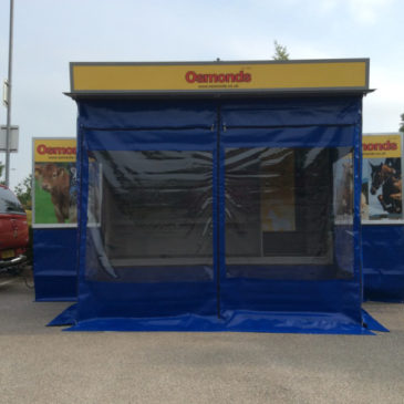 Osmonds take delivery of mobile exhibition shop trailer with ground level open plan display shelving, internal staff seating and kitchen area and wet weather awning, flag poles skirtings and branded 